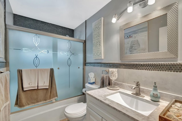 full bathroom featuring vanity, tile walls, toilet, and shower / bath combination with glass door