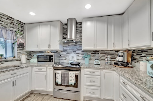 kitchen with stainless steel appliances, backsplash, white cabinets, and wall chimney range hood