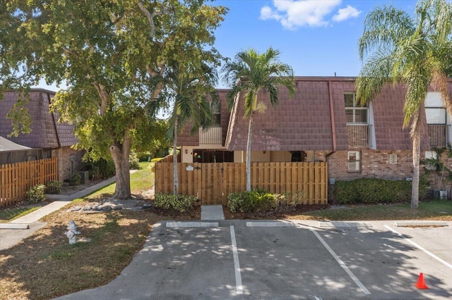 exterior space with mansard roof, brick siding, uncovered parking, and fence