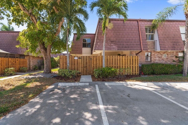 exterior space with mansard roof, brick siding, uncovered parking, and fence