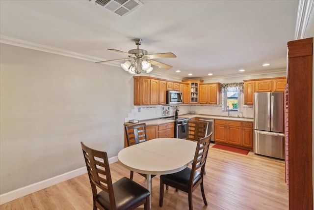 dining room with a ceiling fan, visible vents, baseboards, light wood finished floors, and crown molding