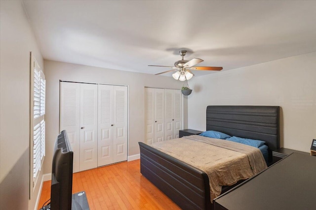 bedroom featuring baseboards, light wood-style flooring, two closets, and ceiling fan