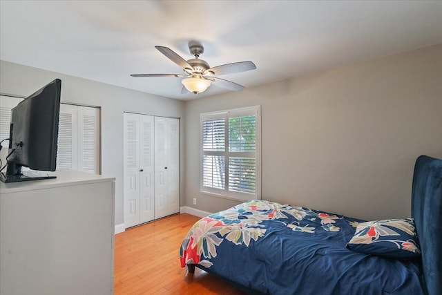 bedroom featuring baseboards, ceiling fan, multiple closets, and light wood finished floors