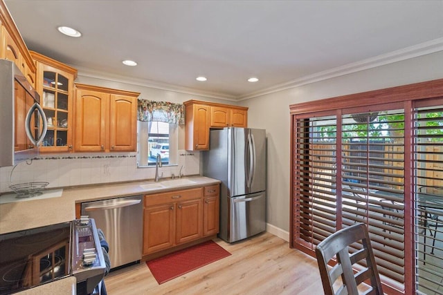 kitchen featuring glass insert cabinets, light wood-type flooring, ornamental molding, appliances with stainless steel finishes, and a sink