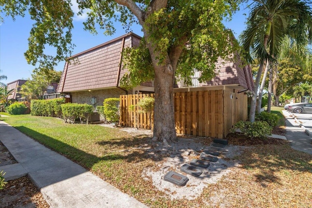 view of side of home featuring mansard roof, fence, brick siding, and a lawn