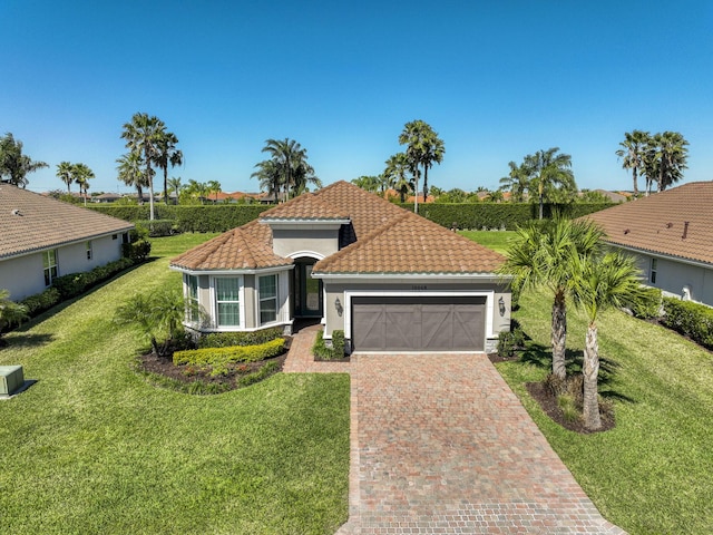 mediterranean / spanish-style home featuring stucco siding, a front lawn, a garage, a tiled roof, and decorative driveway