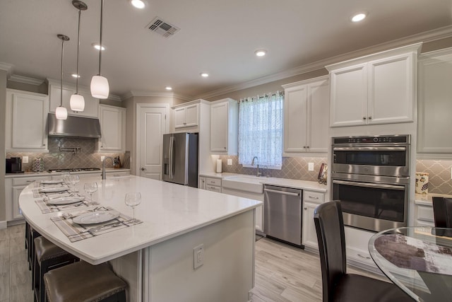 kitchen with visible vents, a breakfast bar, under cabinet range hood, appliances with stainless steel finishes, and white cabinets