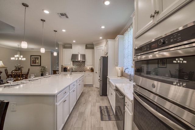 kitchen with visible vents, under cabinet range hood, light countertops, stainless steel appliances, and a sink