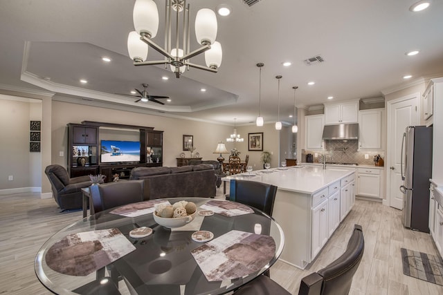 dining room featuring visible vents, ornamental molding, light wood-style flooring, ceiling fan with notable chandelier, and a raised ceiling