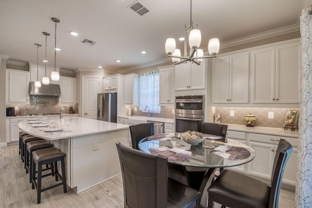 kitchen featuring visible vents, under cabinet range hood, appliances with stainless steel finishes, white cabinetry, and a kitchen island with sink