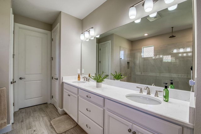 bathroom featuring a sink, tiled shower, wood finished floors, and double vanity