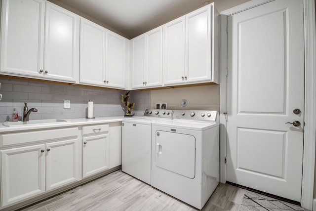 clothes washing area featuring washing machine and clothes dryer, cabinet space, light wood-style floors, and a sink