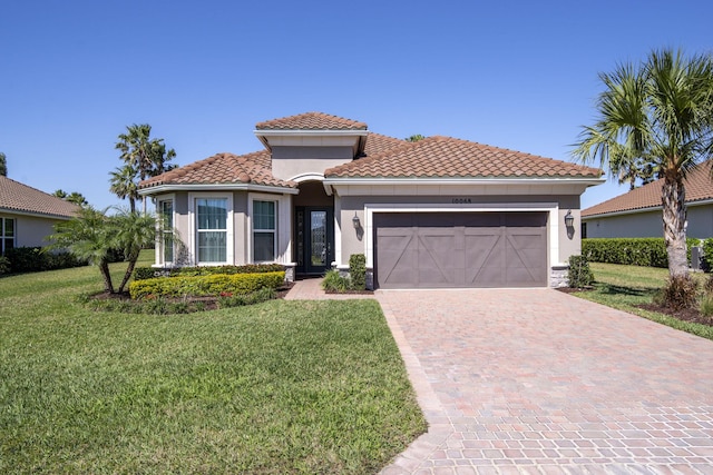 mediterranean / spanish house featuring driveway, stucco siding, a front lawn, a garage, and a tiled roof