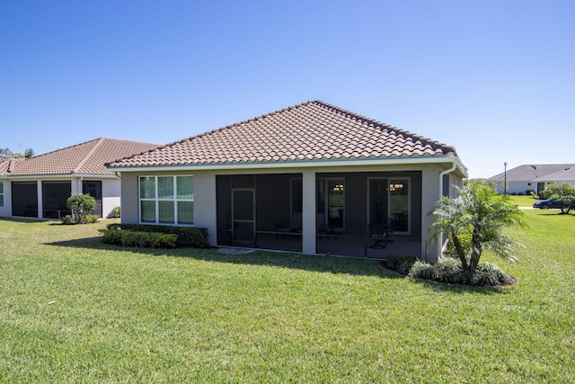 rear view of property featuring stucco siding, a sunroom, a yard, and a tiled roof