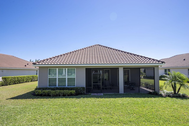 back of property with stucco siding, a tile roof, a lawn, and a sunroom