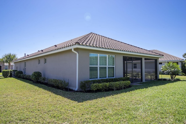 back of house featuring stucco siding, a tile roof, a yard, and a sunroom