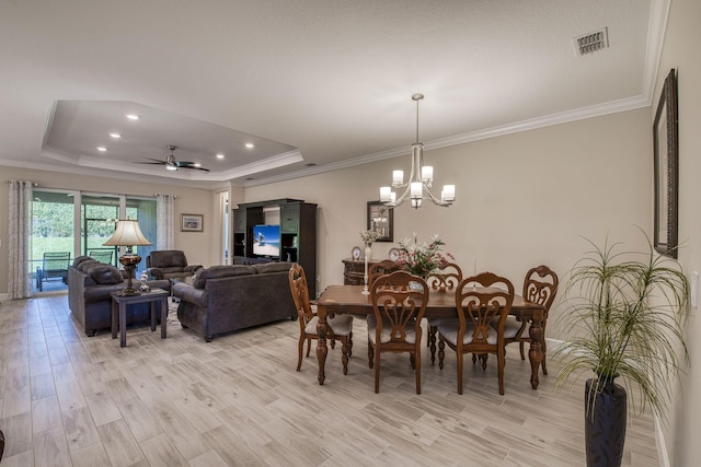 dining room featuring a tray ceiling, light wood-style floors, visible vents, and ceiling fan with notable chandelier