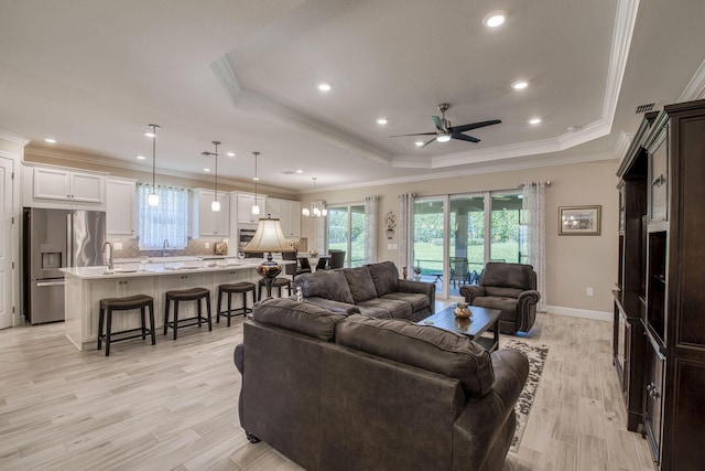 living area with light wood finished floors, crown molding, baseboards, ceiling fan, and a raised ceiling