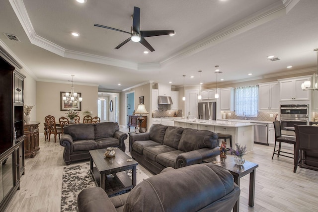 living area with visible vents, ceiling fan with notable chandelier, light wood-style floors, and a tray ceiling