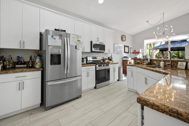 kitchen featuring lofted ceiling, dark stone countertops, white cabinets, stainless steel appliances, and a sink