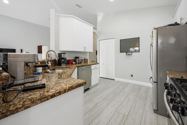 kitchen with wood tiled floor, dark stone counters, appliances with stainless steel finishes, arched walkways, and a sink