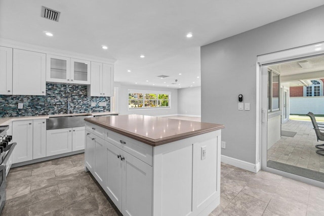 kitchen with tasteful backsplash, visible vents, a center island, white cabinets, and a sink