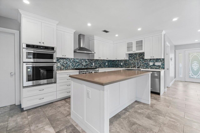 kitchen with stainless steel appliances, wall chimney exhaust hood, a center island, and white cabinetry