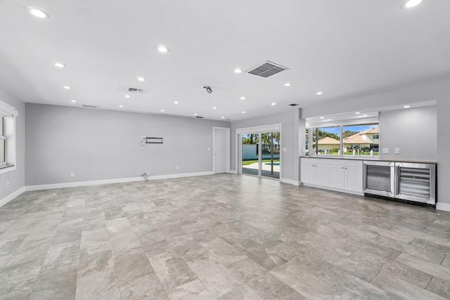 unfurnished living room with visible vents, wine cooler, and baseboards