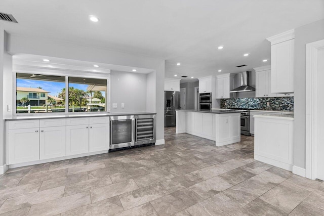 kitchen with tasteful backsplash, wine cooler, appliances with stainless steel finishes, white cabinetry, and wall chimney exhaust hood