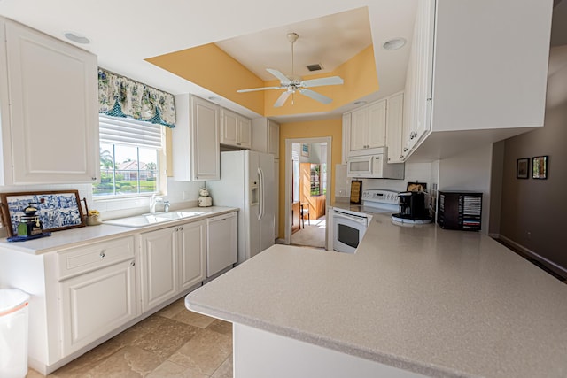 kitchen with white appliances, light countertops, a raised ceiling, and a sink