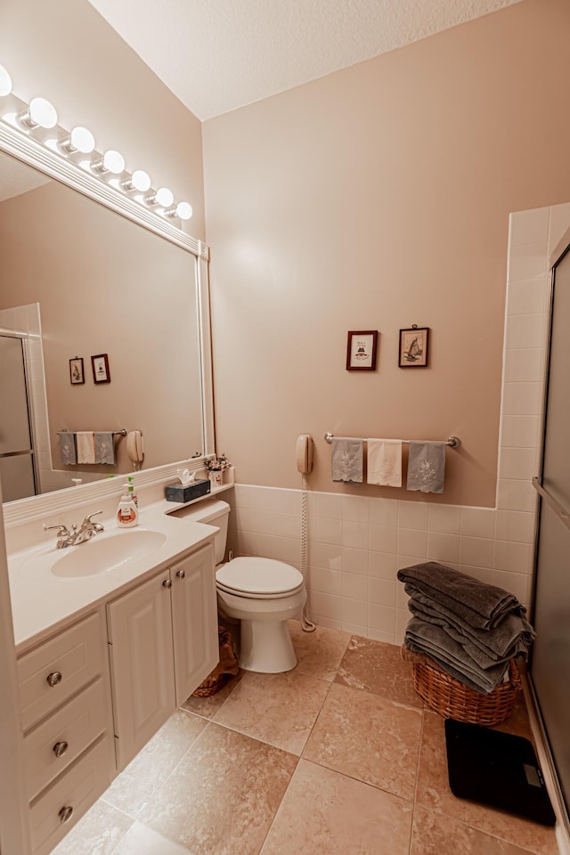 bathroom featuring an enclosed shower, toilet, tile walls, wainscoting, and vanity