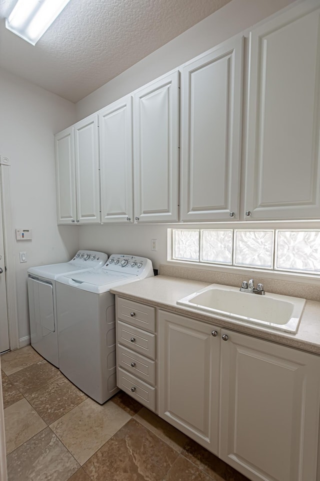 laundry room with washer and dryer, cabinet space, a textured ceiling, and a sink