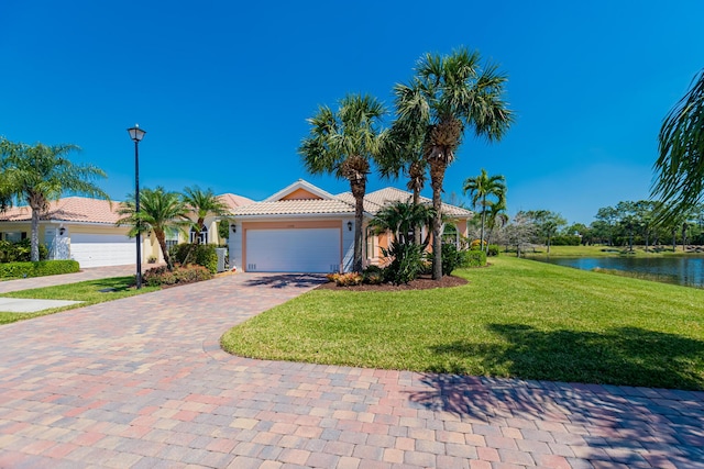 view of front of home with an attached garage, a front lawn, a water view, a tile roof, and decorative driveway