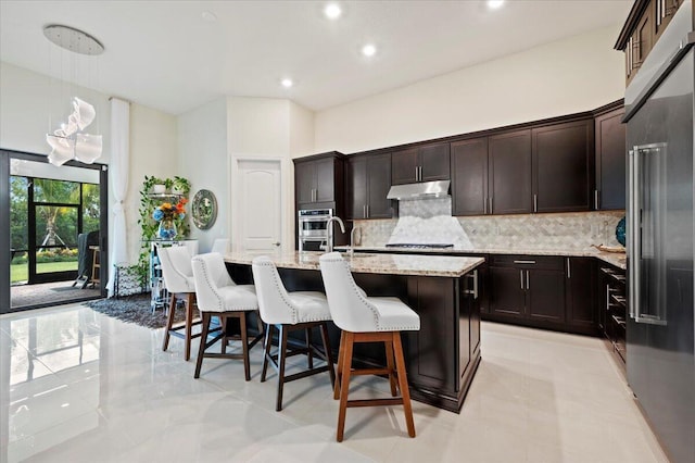 kitchen featuring a kitchen island with sink, under cabinet range hood, a kitchen breakfast bar, tasteful backsplash, and stainless steel appliances