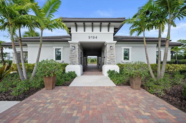 doorway to property with stucco siding, stone siding, fence, and a gate