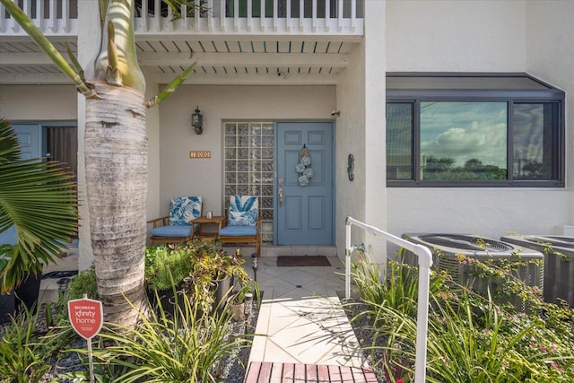 view of exterior entry with stucco siding, a balcony, and central AC unit