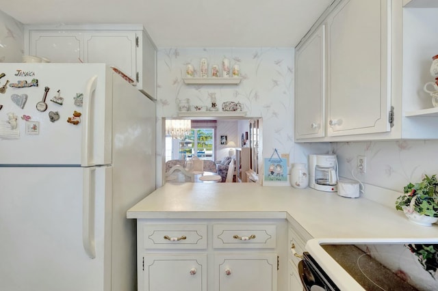 kitchen featuring wallpapered walls, freestanding refrigerator, range with electric cooktop, light countertops, and white cabinets