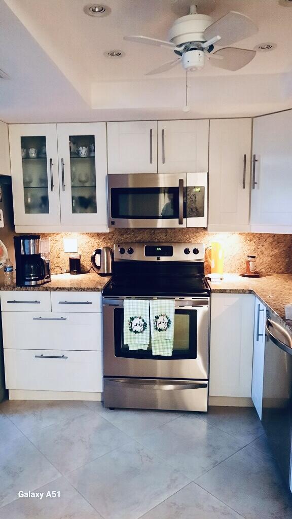 7365 NW 18th St Unit 107, Margate, FL 33063 - kitchen with appliances with stainless steel finishes, white cabinetry, glass insert cabinets, and backsplash
