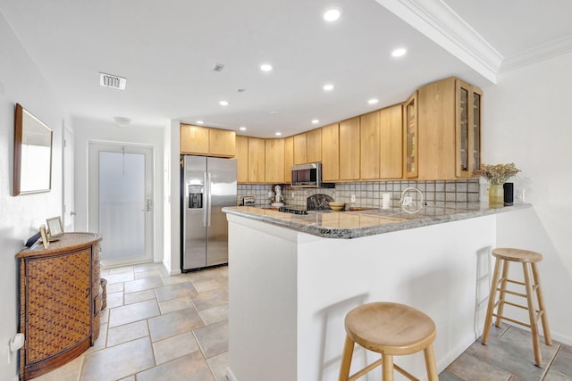 kitchen with light stone counters, tasteful backsplash, appliances with stainless steel finishes, a breakfast bar area, and a peninsula