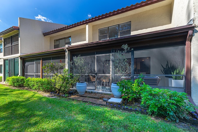 back of property with a lawn, a sunroom, and stucco siding