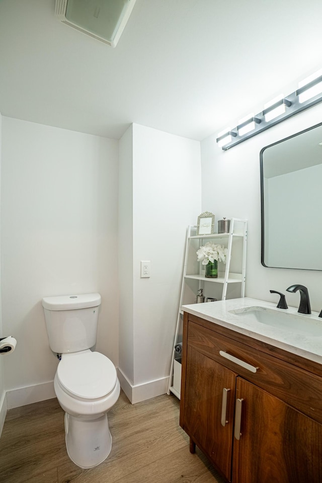 half bathroom featuring baseboards, toilet, wood finished floors, and vanity