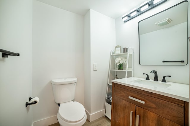 half bathroom featuring visible vents, baseboards, toilet, wood finished floors, and vanity