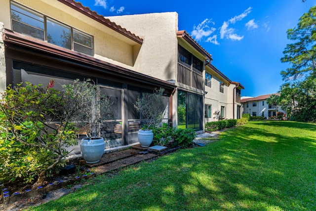 back of property featuring stucco siding, a sunroom, a lawn, and a tile roof