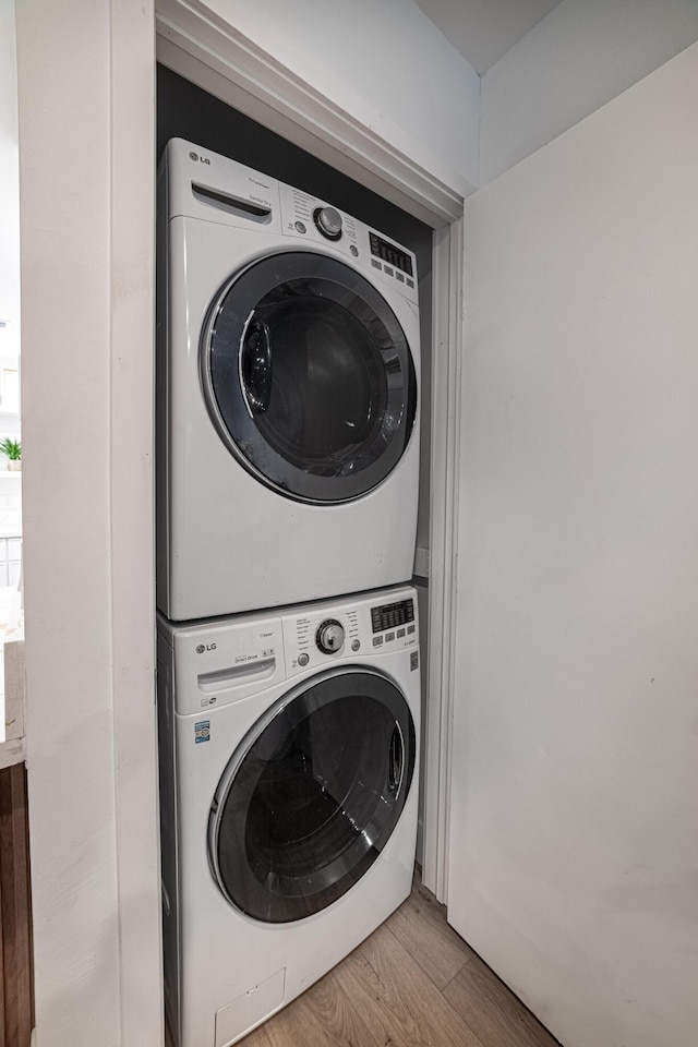 clothes washing area with stacked washer and dryer, wood finished floors, and laundry area