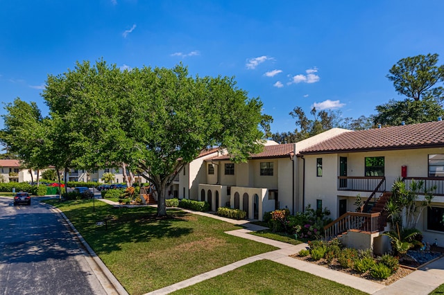 exterior space with stairway, a residential view, a tile roof, a front yard, and stucco siding