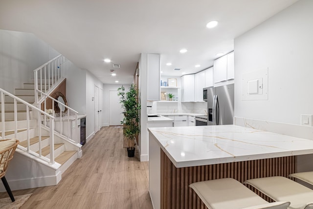 kitchen featuring light wood finished floors, a peninsula, stainless steel appliances, white cabinetry, and open shelves