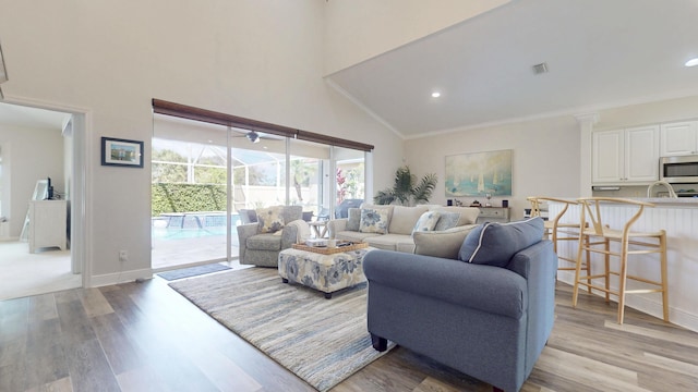 living area featuring visible vents, high vaulted ceiling, light wood-style flooring, and ornamental molding