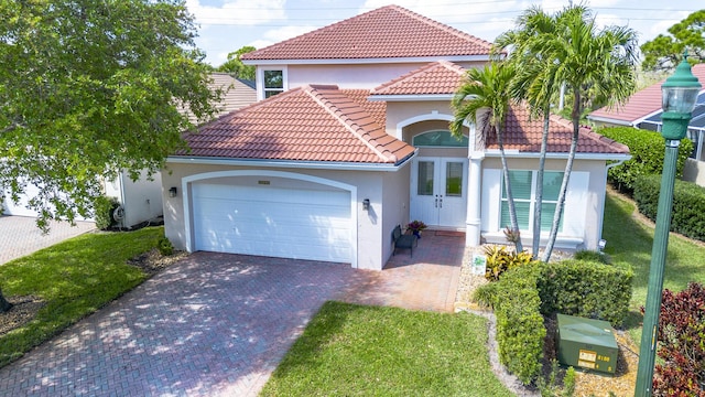 mediterranean / spanish house with stucco siding, driveway, a tile roof, french doors, and an attached garage