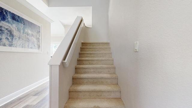 stairway with wood finished floors, baseboards, and a textured wall