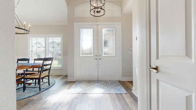 entryway with a notable chandelier, ornamental molding, and wood finished floors